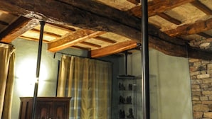 Ein Zimmer mit freiliegenden Holzbalken, einer Steinwand und einer Glasschrank mit Figuren.