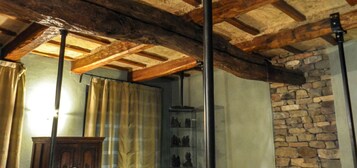 Una habitación con vigas de madera a la vista, pared de piedra y un aparador de vidrio con figuritas.
