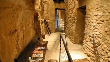 Un estrecho pasillo de piedra con un banco de madera y una escalera apoyada en la pared.