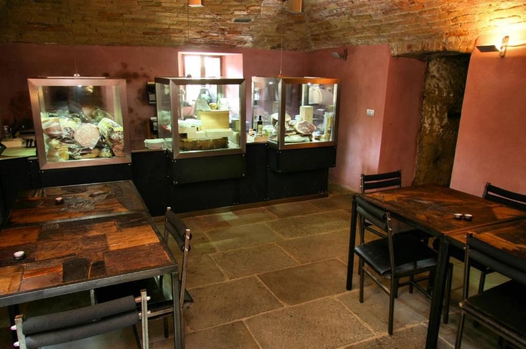 Restaurante com chão de pedra, mesas de madeira e vitrines de vidro com alimentos.