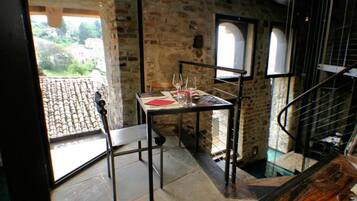 A dining area with a table set for two, a chair, and a view of a courtyard through a window.