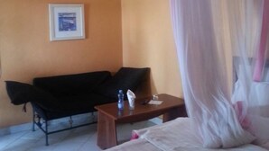 A hotel room with a bed, a small table, a sofa, and a picture on the wall. - Genesis Guest House (Naivasha)