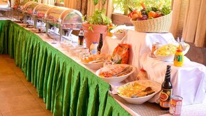 A buffet setup with various food items and condiments, a potted plant, and a bottle on the table. - Genesis Guest House (Naivasha)