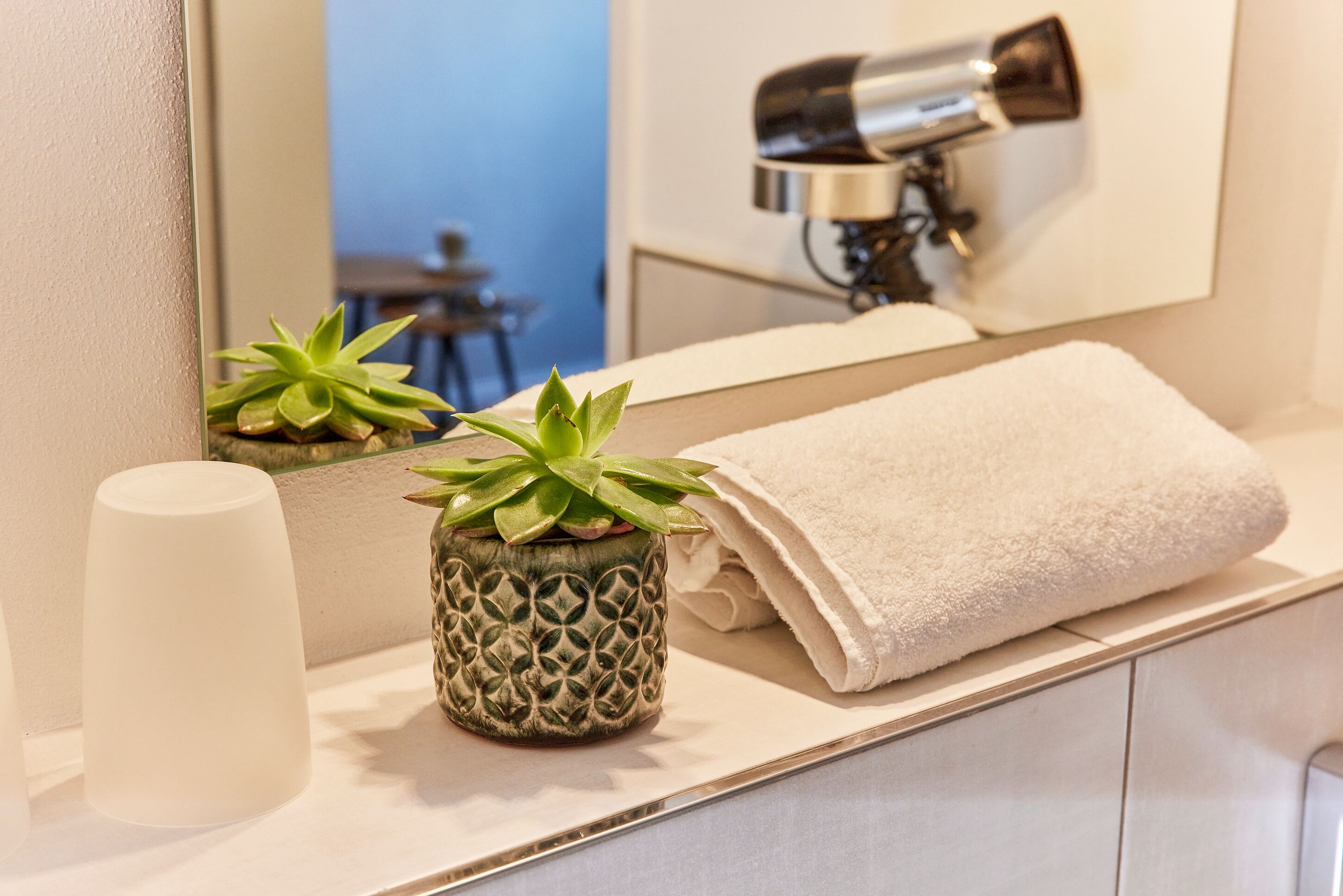 Un baño con una toalla blanca, una planta en maceta y un secador de pelo en el espejo.