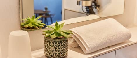 A bathroom with a white towel, a potted plant, and a hairdryer in the mirror.