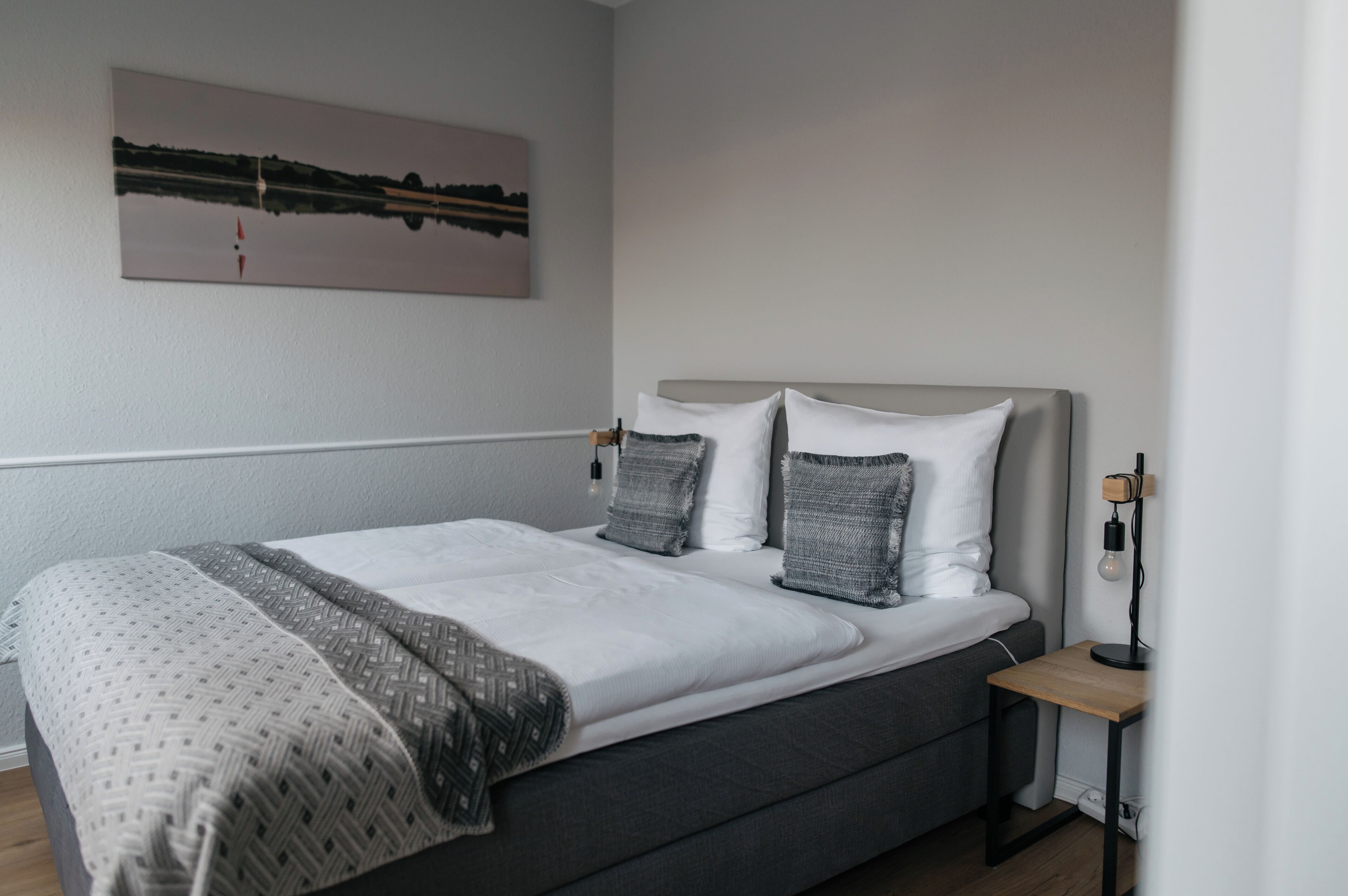 A modern bedroom with a large bed, a bedside table, and a wall-mounted lamp.