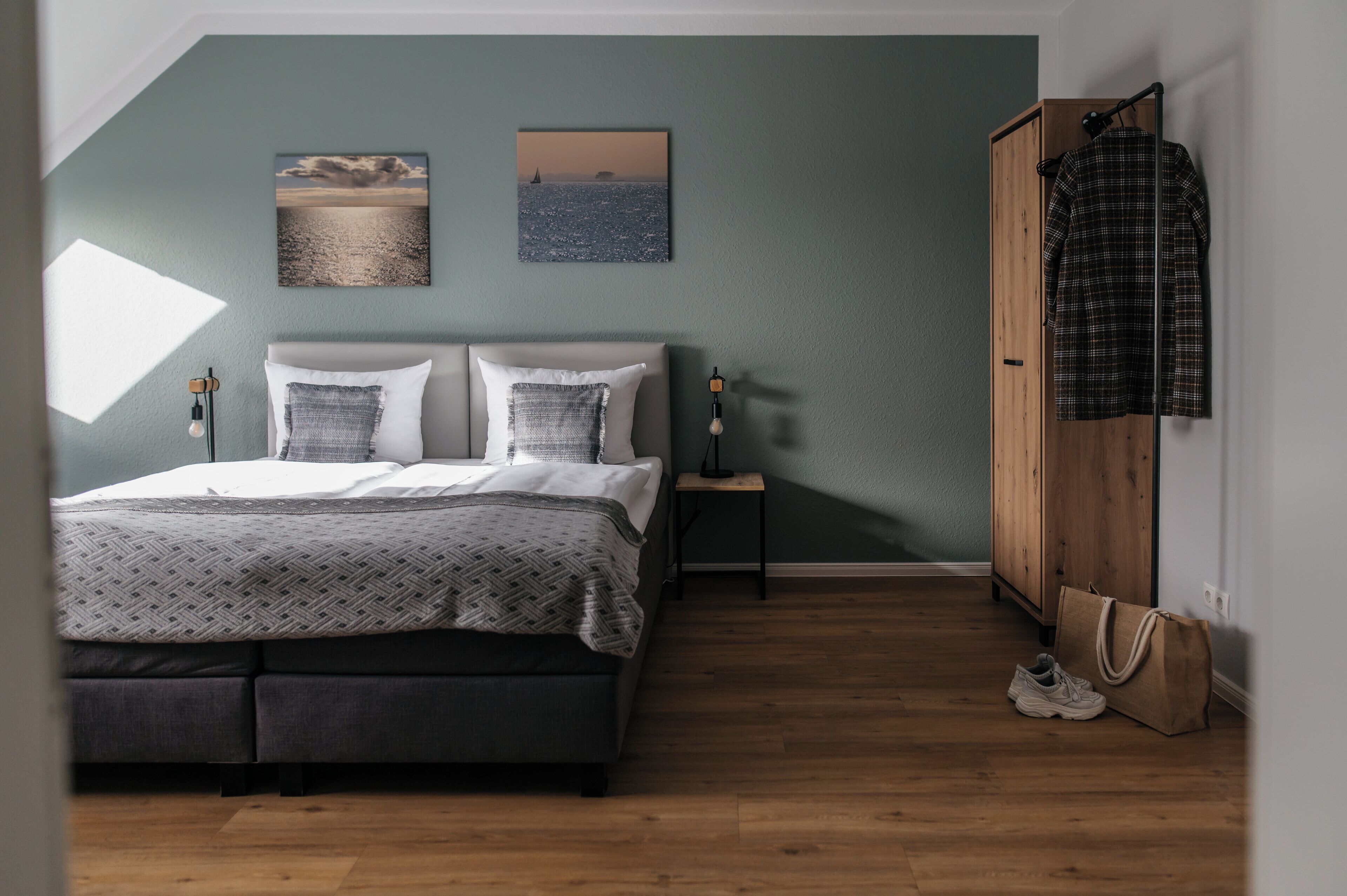Un dormitorio con una cama, dos almohadas, una mesita de noche, un armario de madera y un par de zapatos.
