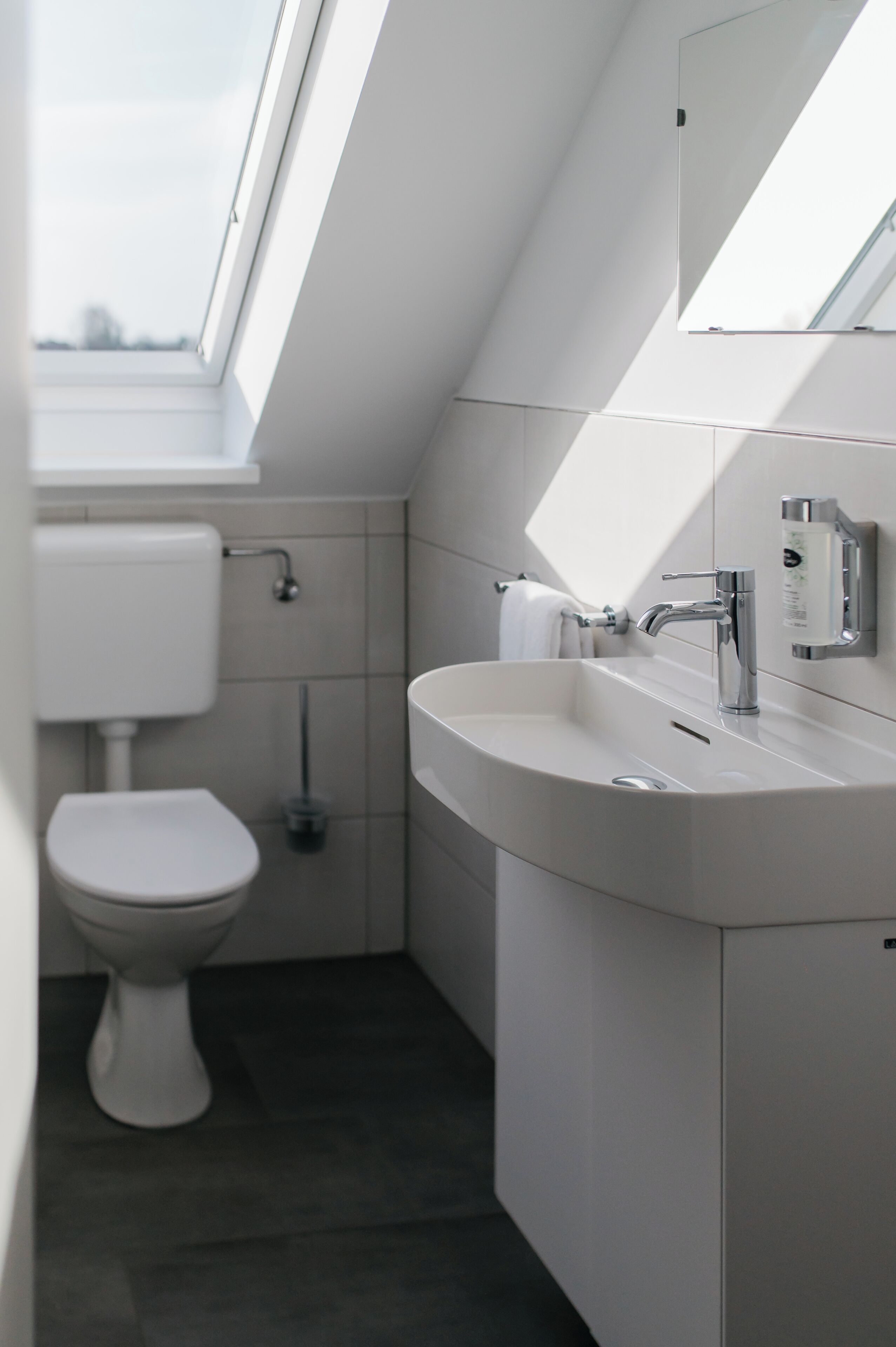 A modern bathroom with a skylight, a toilet, a sink, and a mirror.