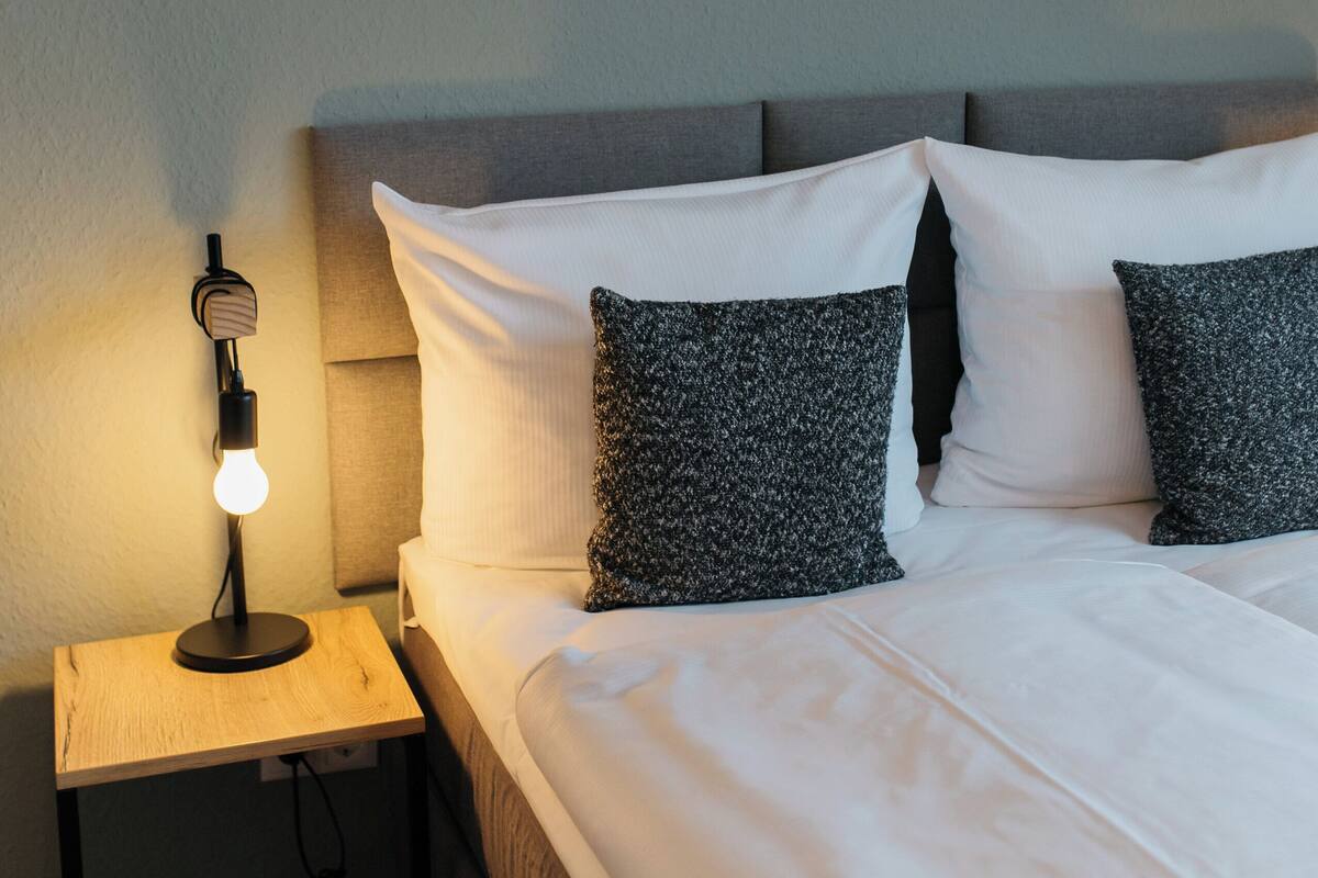Une chambre à coucher avec un lit, des oreillers, une table de chevet avec une lampe et un tableau accroché au mur.