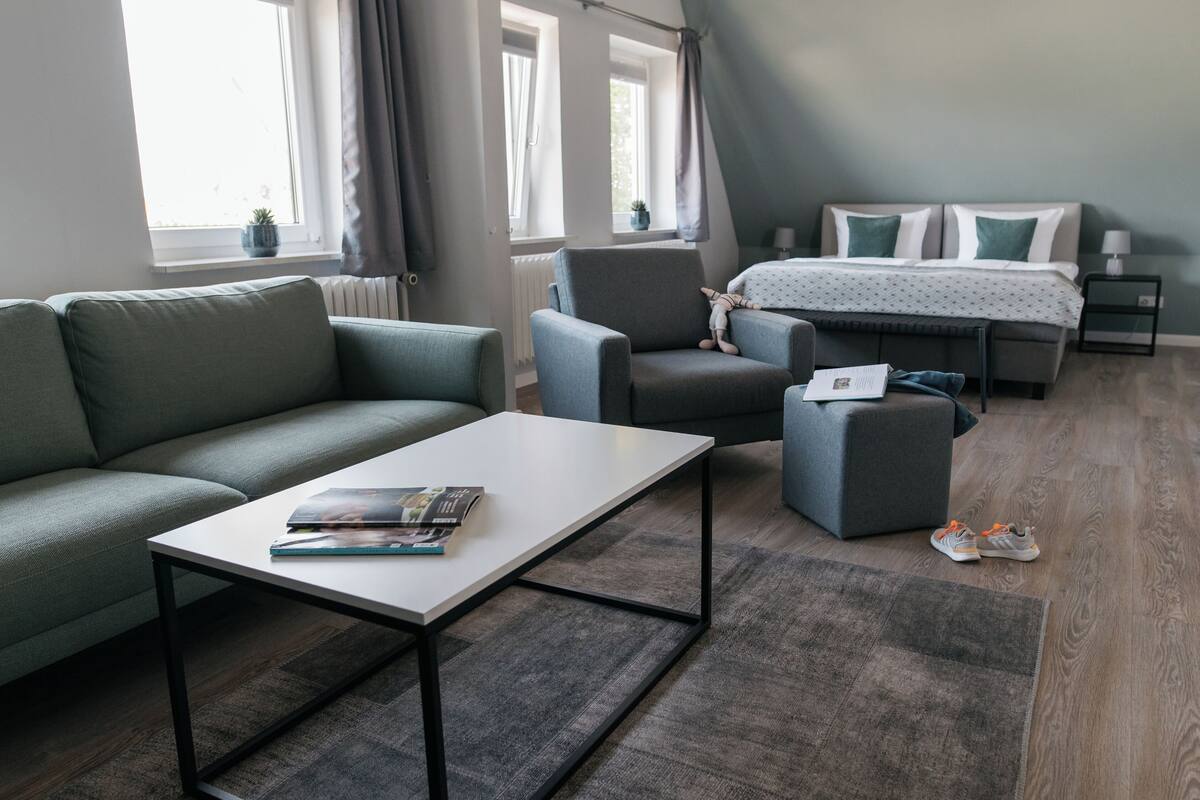 Une pièce moderne et bien éclairée, avec un canapé, un fauteuil et un lit recouvert d’une couvre-lit à motifs.