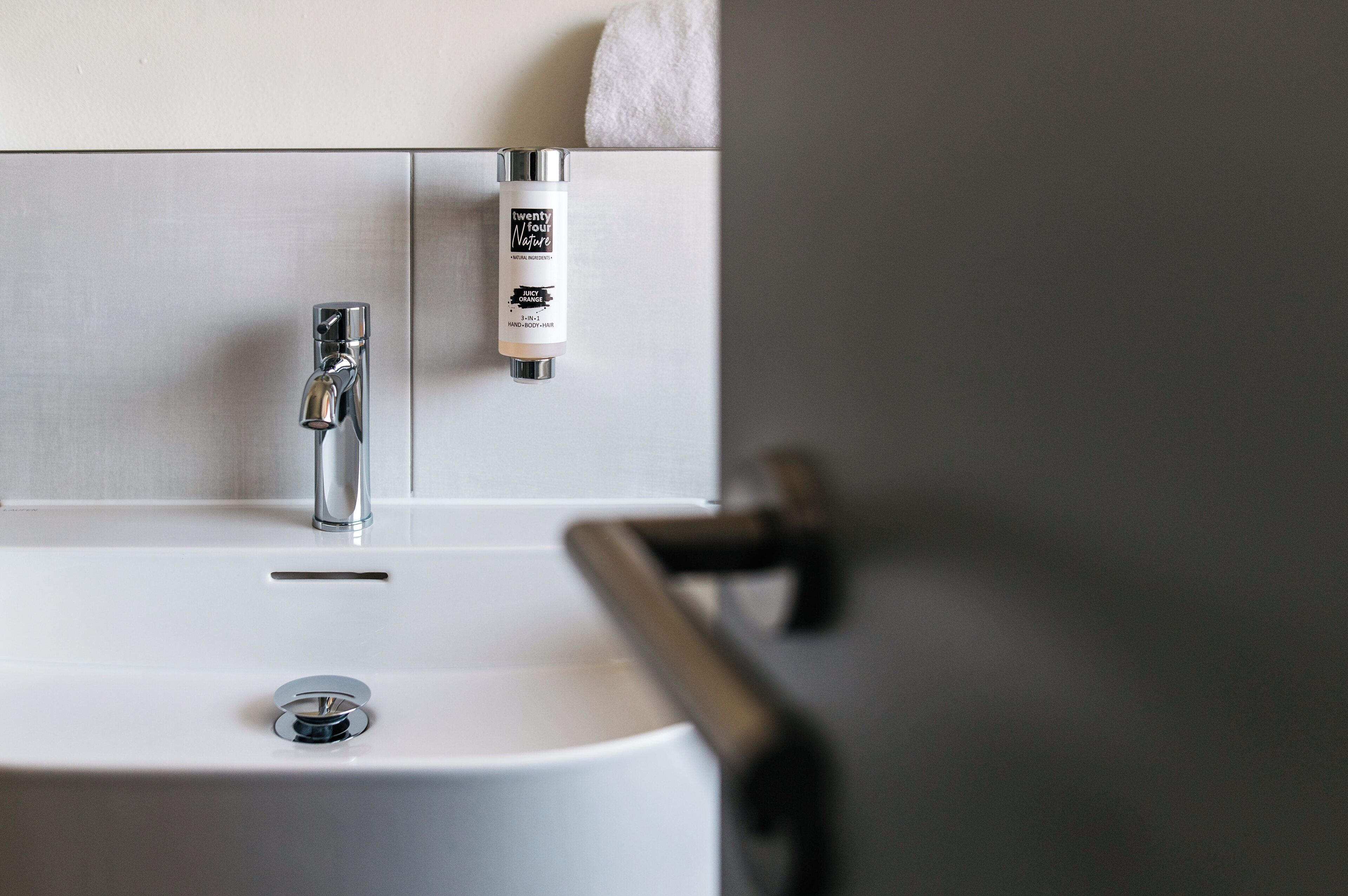 Ein Waschtisch mit chromfarbenem Wasserhahn, einer Handseifenflasche und einem Handtuch, das an der Wand hängt.