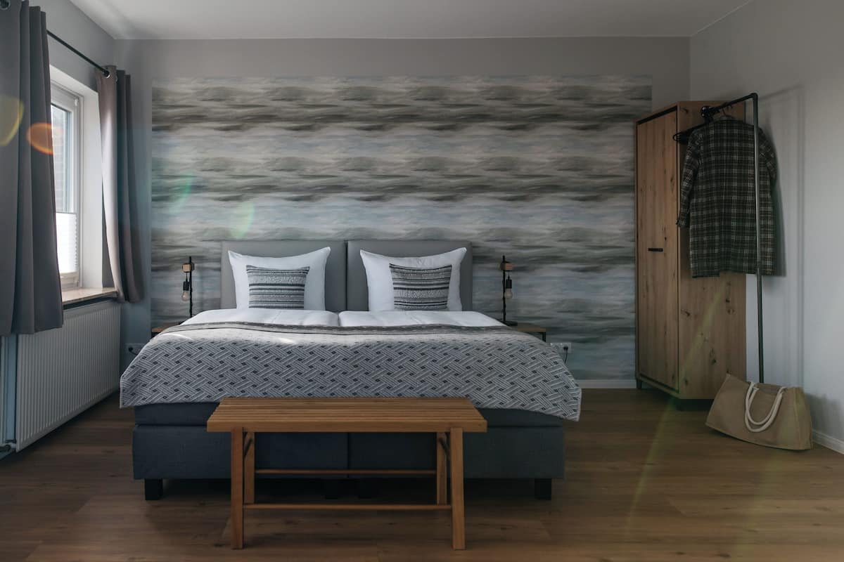 Une chambre à coucher avec un lit, un banc, une armoire et une fenêtre avec des rideaux.
