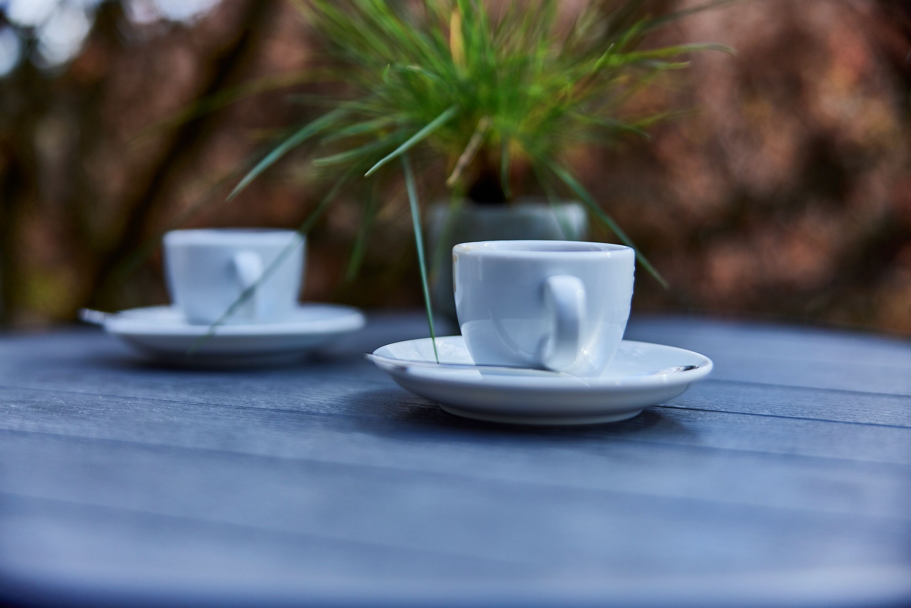 Two white cups on saucers on a blue table.