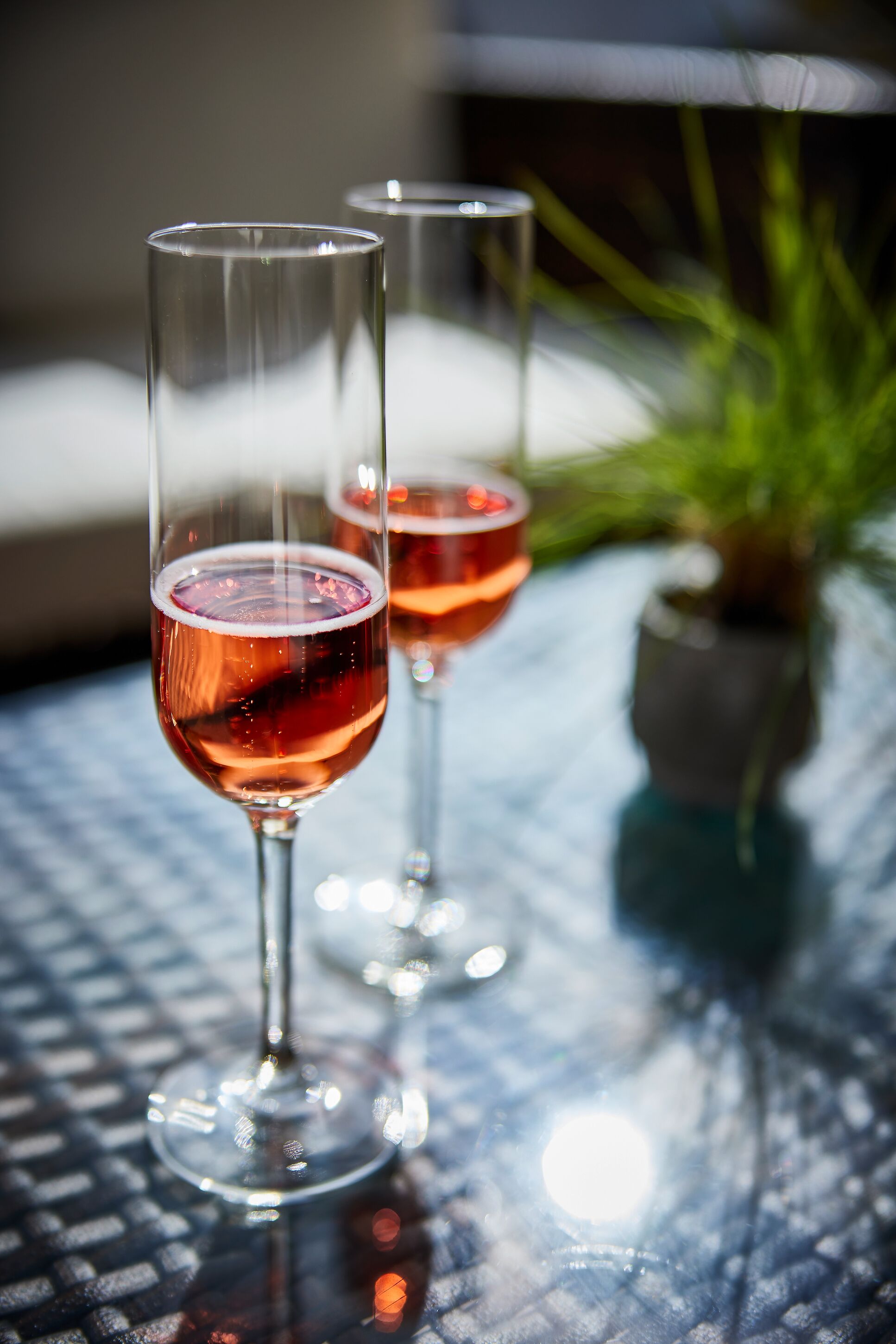 Two glasses of red wine on a glass table with a blurred background.