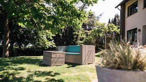 Een terras met een bank en tafel, omgeven door weelderige begroeiing en bomen.