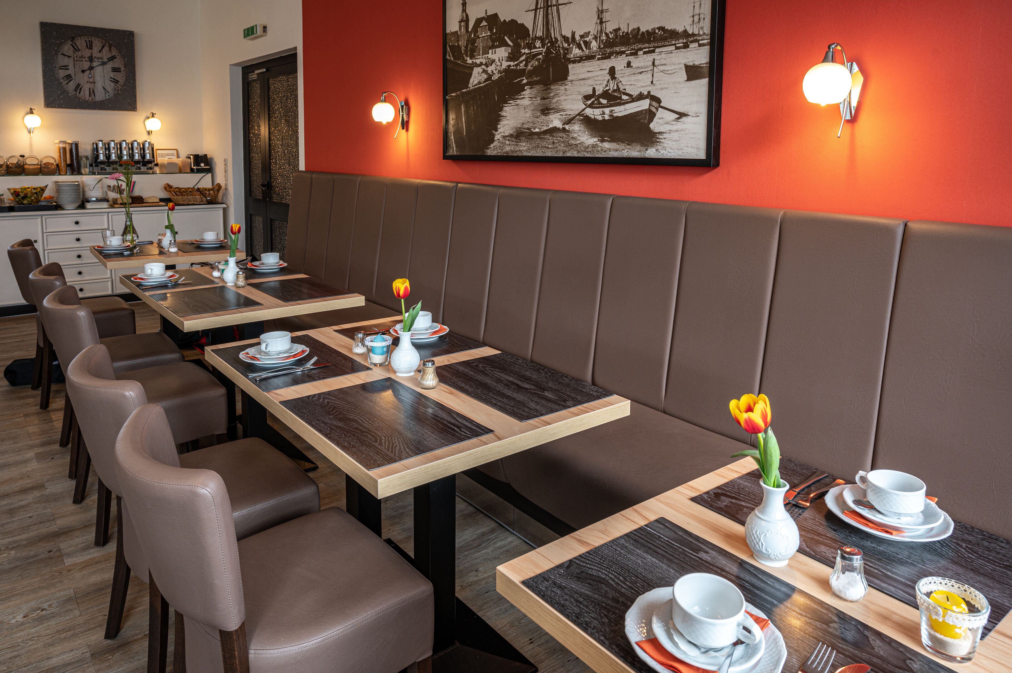 Un restaurante con cabinas y mesas, cada conjunto con platos, vasos y jarrones con flores.