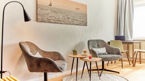 Een moderne woonkamer met twee fauteuils, een kleine ronde tafel met een plant en een kopje, en een schilderij van een zeilboot aan de muur.