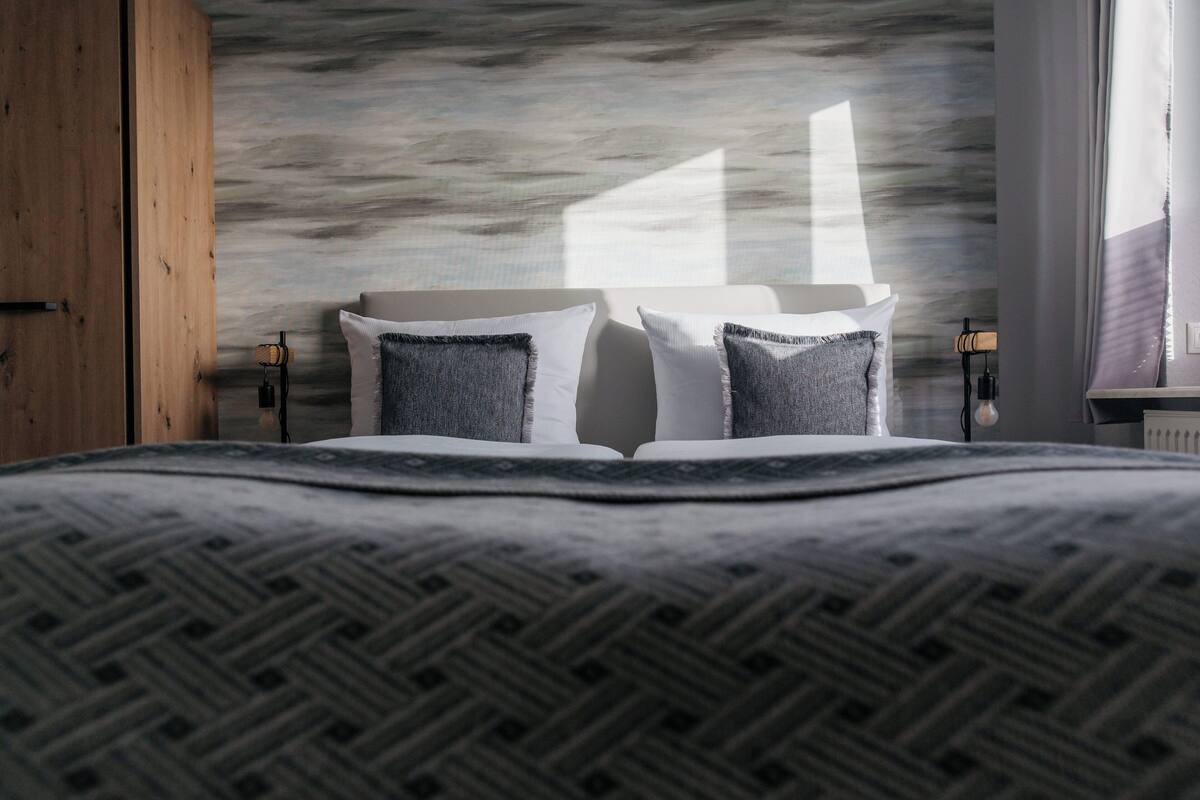 Un lit bien fait, avec une couvre-lit à motifs, une tête de lit agrémentée de deux oreillers et un mur orné d’un motif texturé.