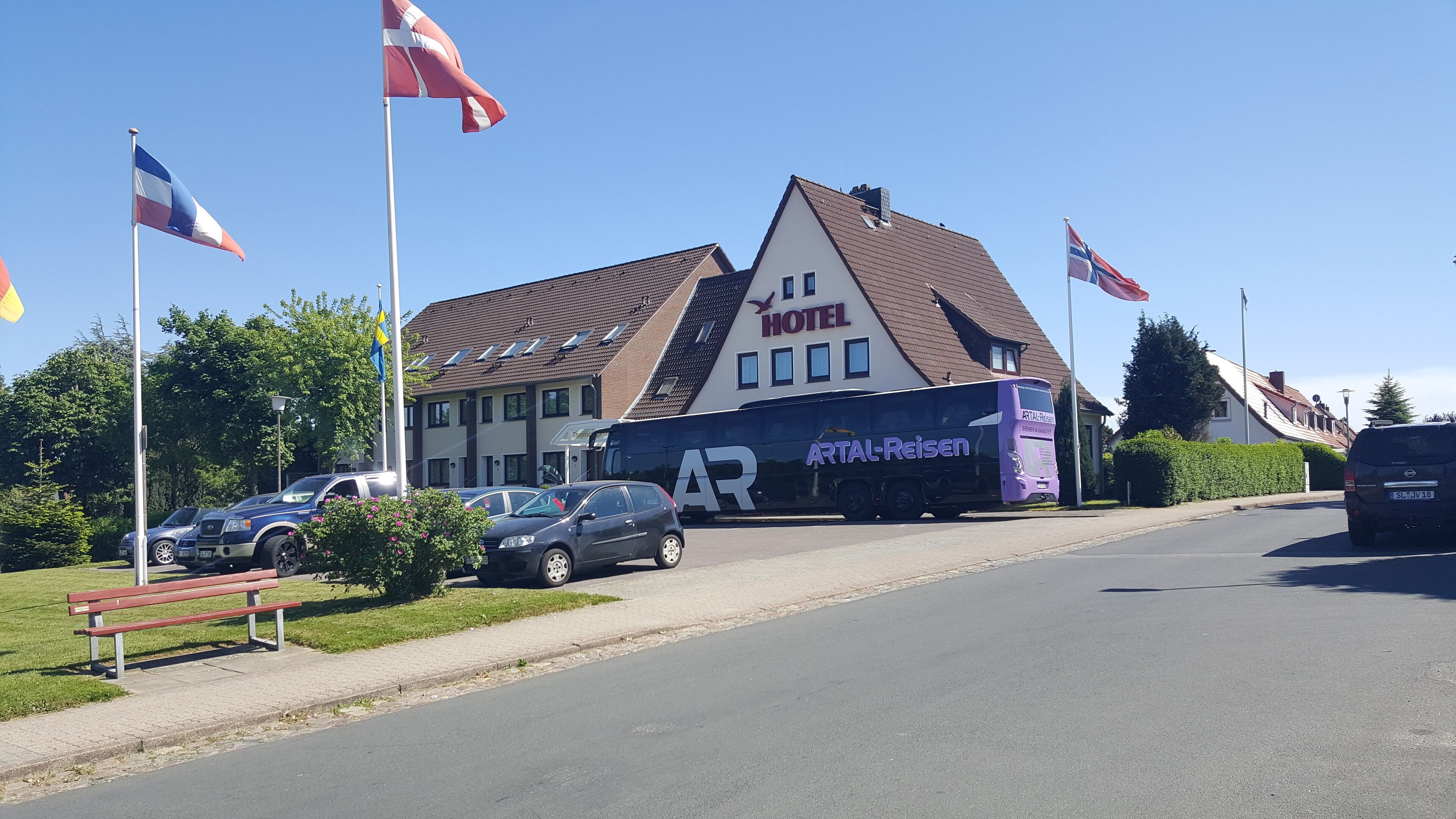 A hotel with a prominent 'HOTEL' sign, a parked bus, and multiple flags.