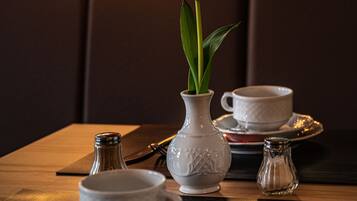 A dining table set with a white cup, saucer, and a small vase with a single tulip.