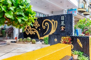 A hotel entrance with a black wall featuring gold decorative elements and Chinese characters. There are potted plants and a yellow bench in the foreground.