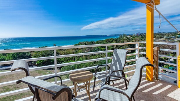 Un balcon avec vue sur l’océan, agrémenté de fauteuils en osier et d’une petite table.