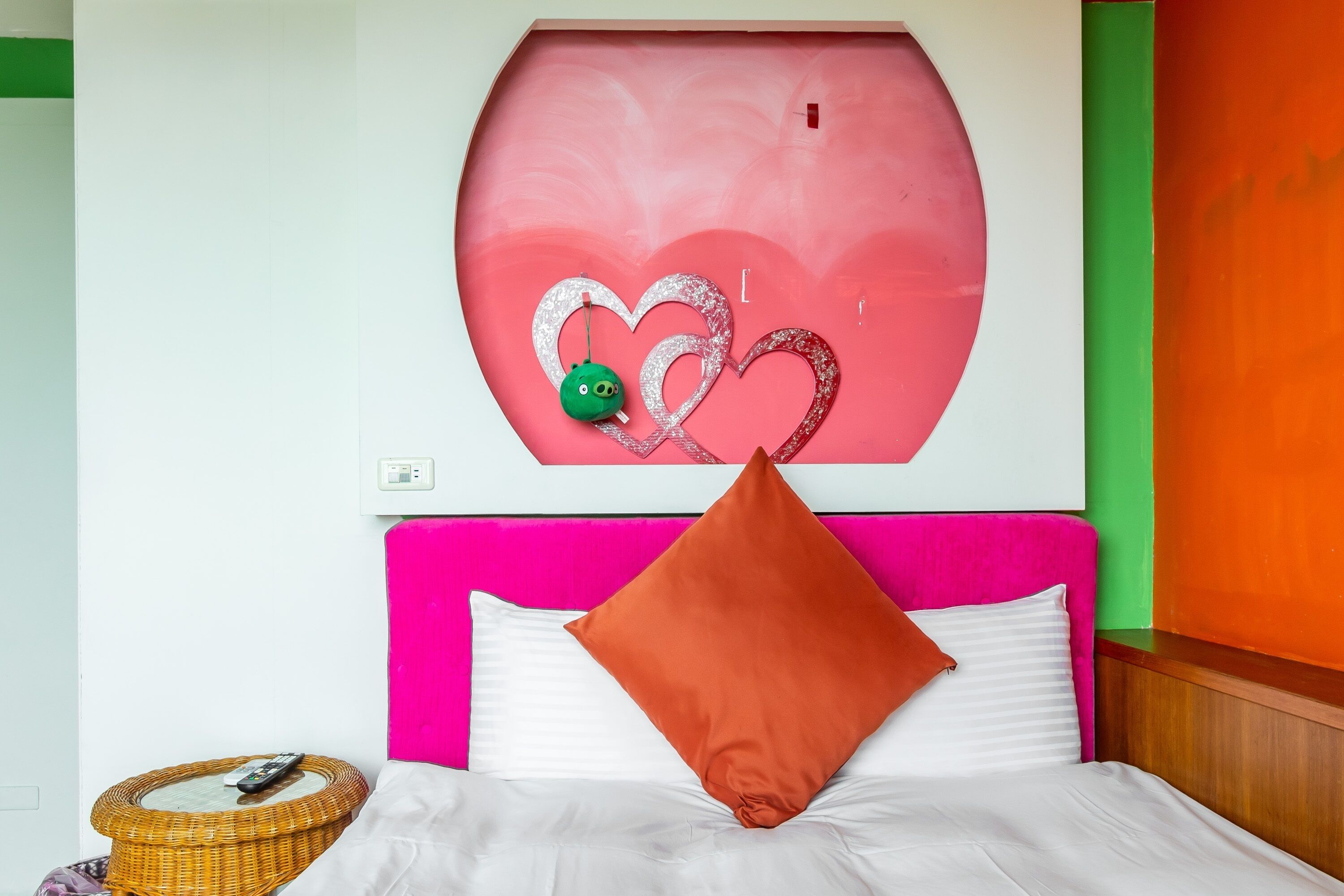 Una cama con ropa blanca, cabecera rosa y un adorno de pared con corazones.