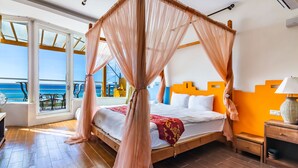 Une chambre à coucher avec un lit à baldaquin, une table de chevet en bois et une vue sur l’océan grâce à de grandes fenêtres.