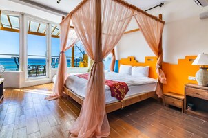 A bedroom with a four-poster bed, a wooden nightstand, and a view of the ocean through large windows.