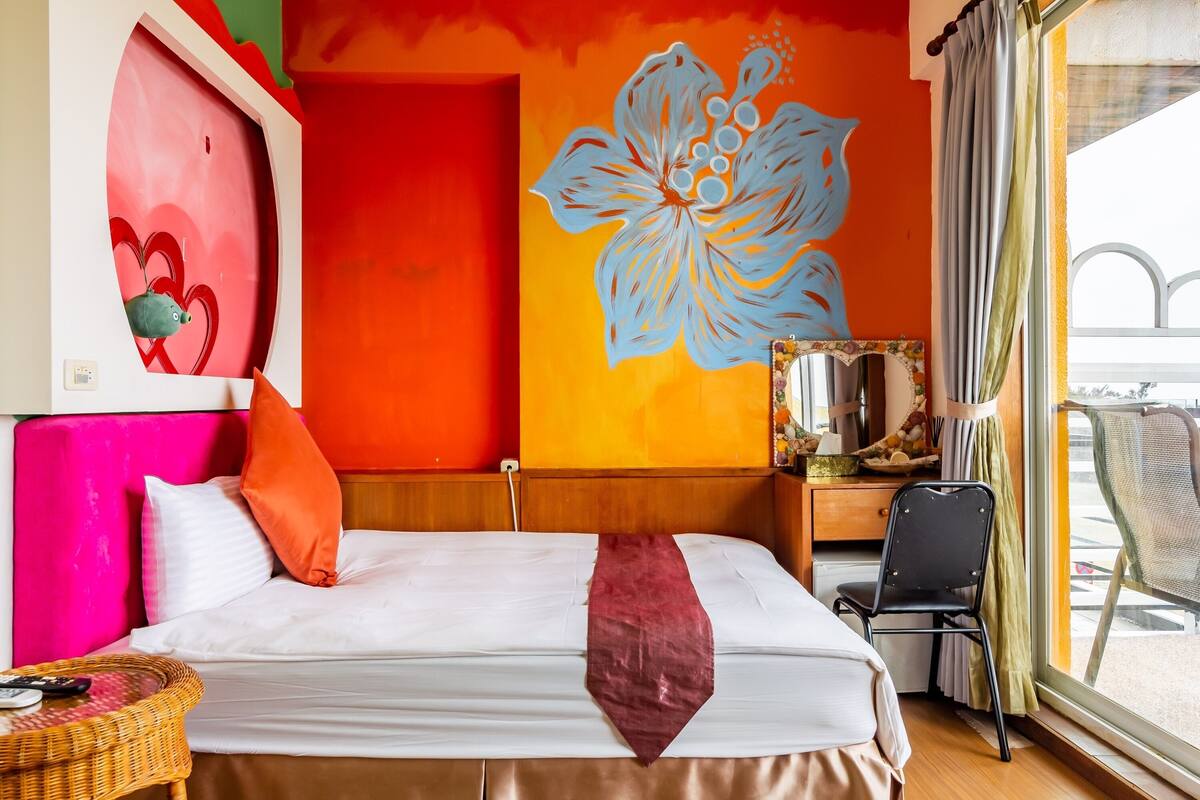 A hotel room with a bed, a desk, a chair, and a large window.