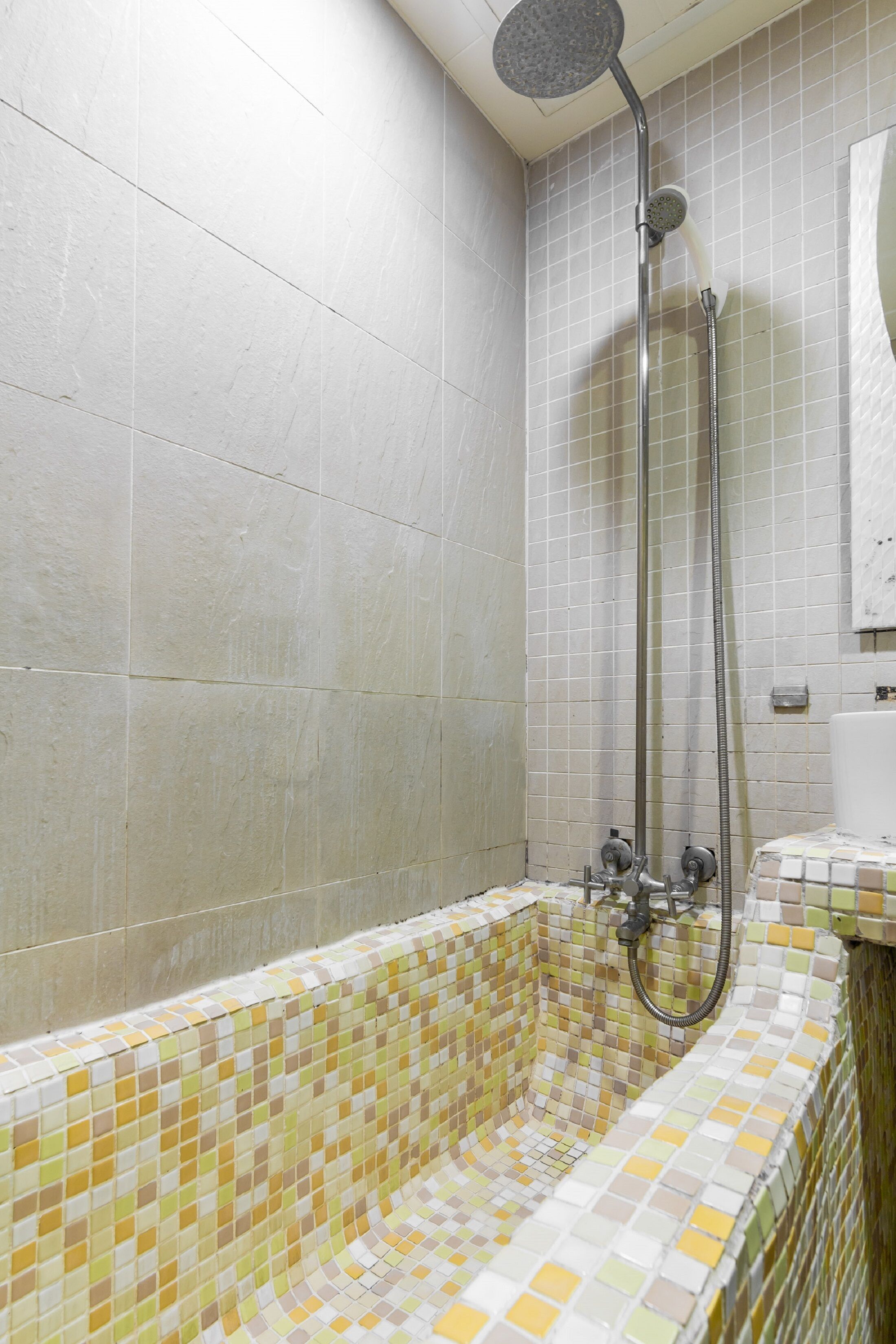 A bathroom with a tiled shower area and a mosaic-tiled bathtub.