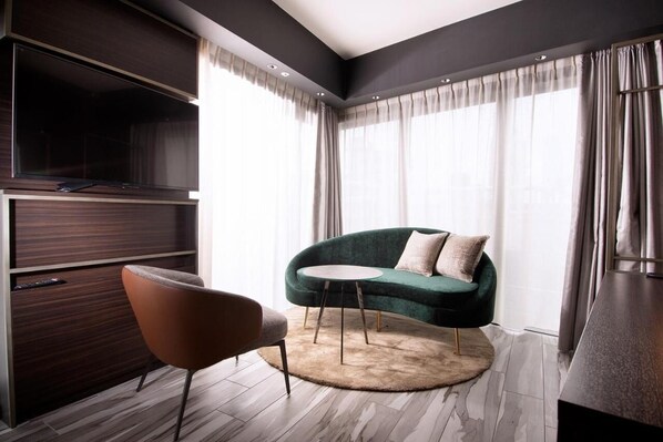 A modern living room with a dark wood cabinet, a green sofa, a round coffee table, and a brown armchair. - Kobe Plaza Hotel West (Kobe)