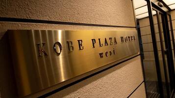 A metallic plaque with the text 'KOBE PLAZA HOTEL west' on a textured wall.