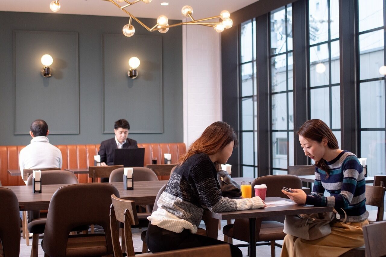 A modern dining area with wooden tables and booths, large windows, and pendant lighting.