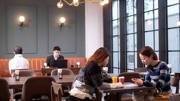 A modern dining area with wooden tables and booths, large windows, and pendant lighting.