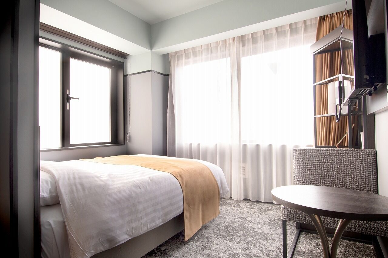A hotel room with a bed, a round table, and a window with curtains.