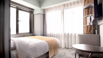 A hotel room with a bed, a round table, and a window with curtains.