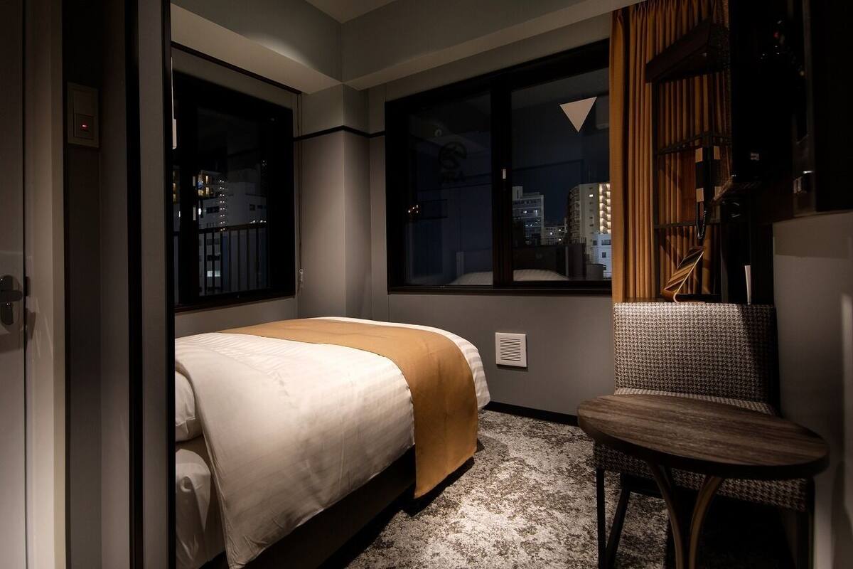 Quarto de hotel com cama, cadeira e janela vista para a cidade.