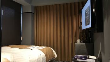 Ein Hotelzimmer mit einem Bett, einem an der Wand montierten Fernseher, einem kleinen Tisch mit einem Laptop und einem Fenster mit Vorhängen.