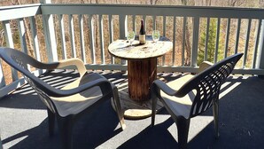Eine Holzterrasse mit einem runden Tisch und zwei Stühlen mit Blick auf einen bewaldeten Bereich.