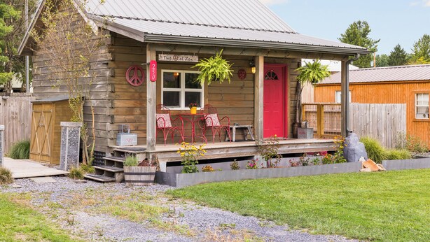 En rustik træhytte med en rødlakeret dør, en veranda med røde stole og et skilt, der siger "The Inn of Zen".