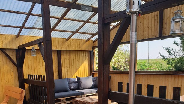 An outdoor patio with a metal stove, wooden furniture, and a view of the surrounding landscape. - Gulfhof (Emden)