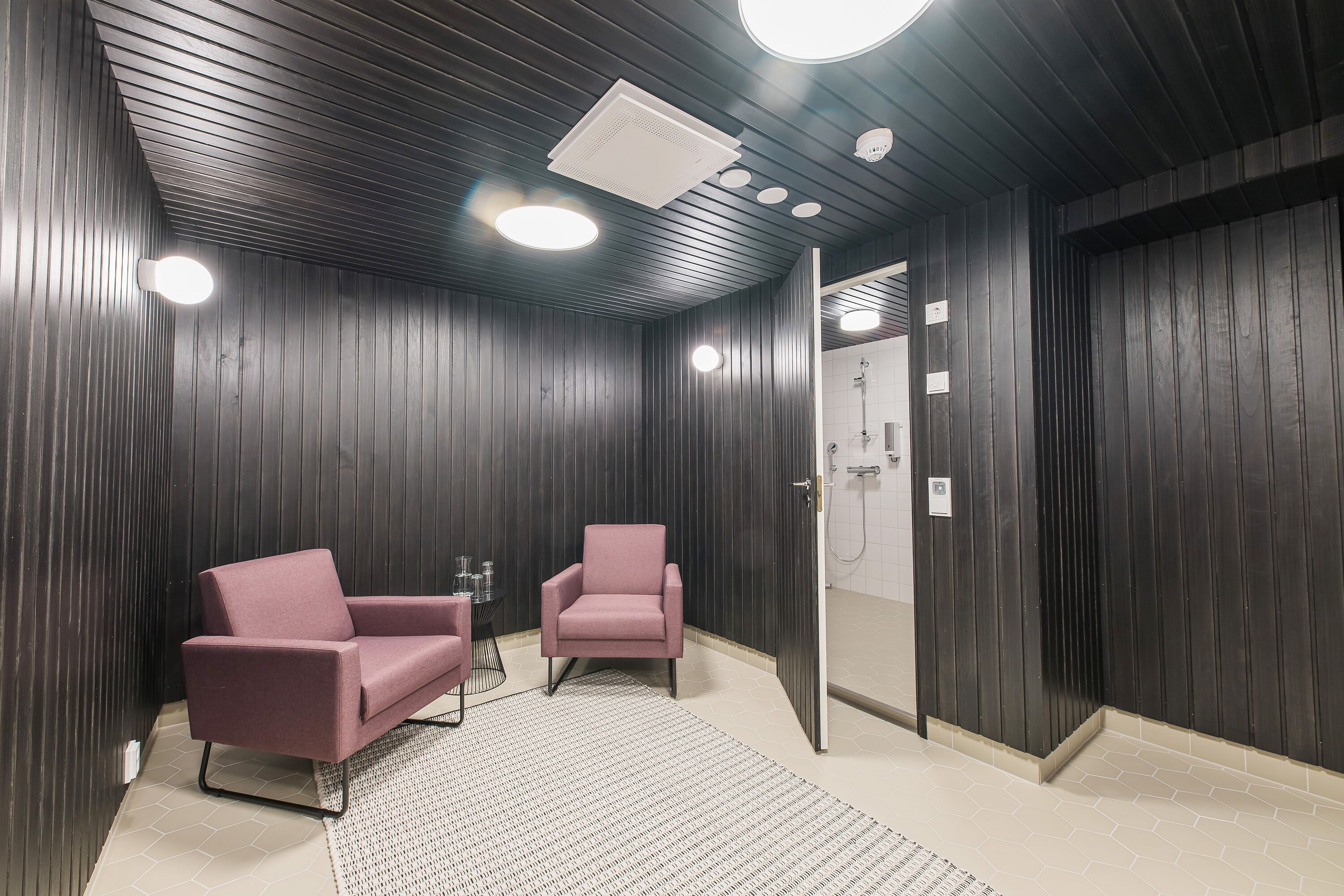 Une pièce moderne avec des murs en bois foncé, deux fauteuils roses, une petite table et un luminaire au plafond.
