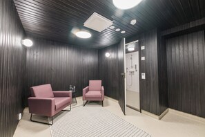 A modern room with dark wooden walls, two pink armchairs, a small table, and a ceiling light fixture. - Forenom Aparthotel Jyväskylä (Jyväskylä)