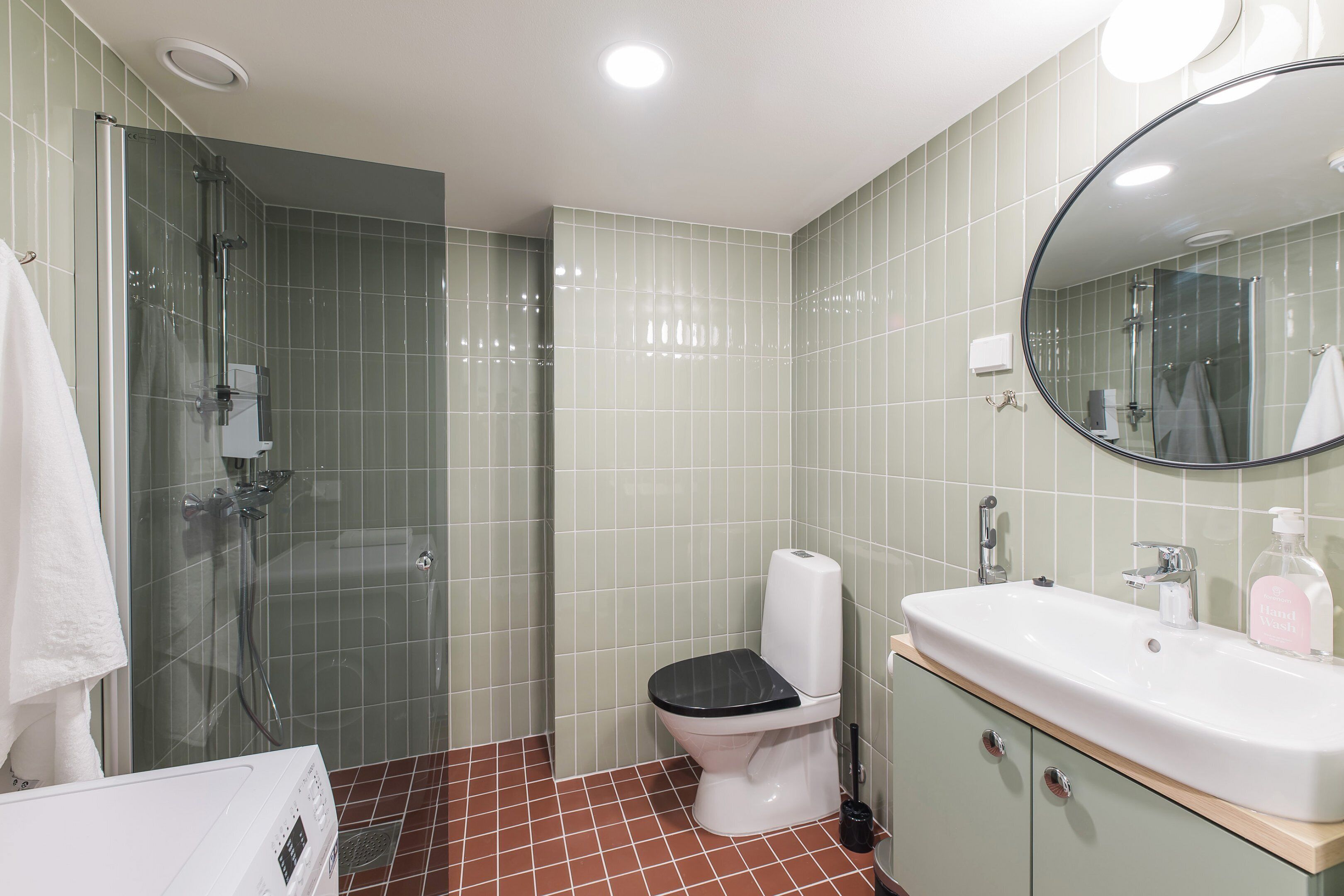 A bathroom with a glass-enclosed shower, a toilet, and a sink with a mirror above it.