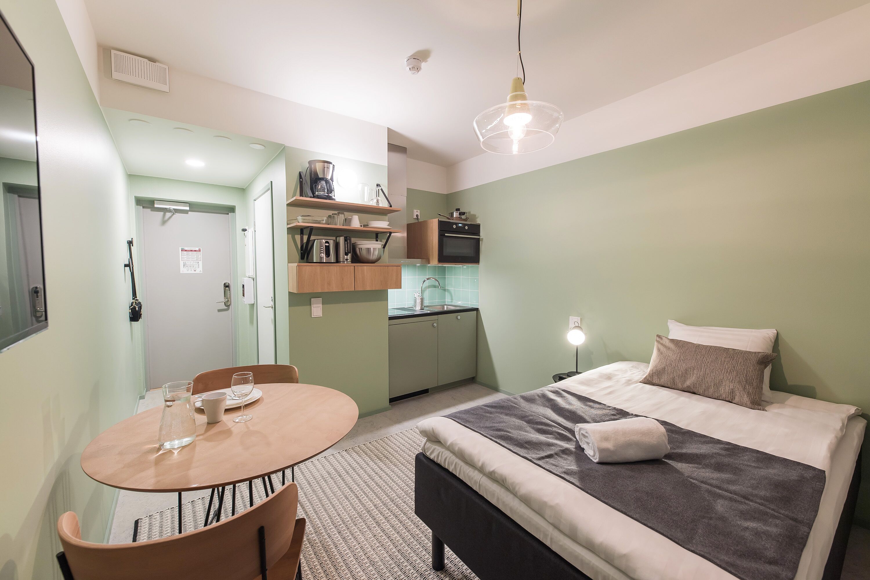 Una habitación pequeña con cama, mesa de comedor y kitchenette.