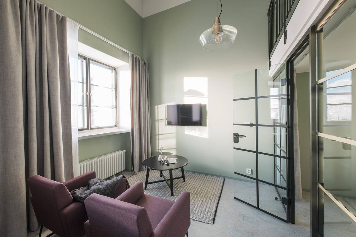 A modern room with a large window, a flat-screen TV, a round table, and two armchairs.