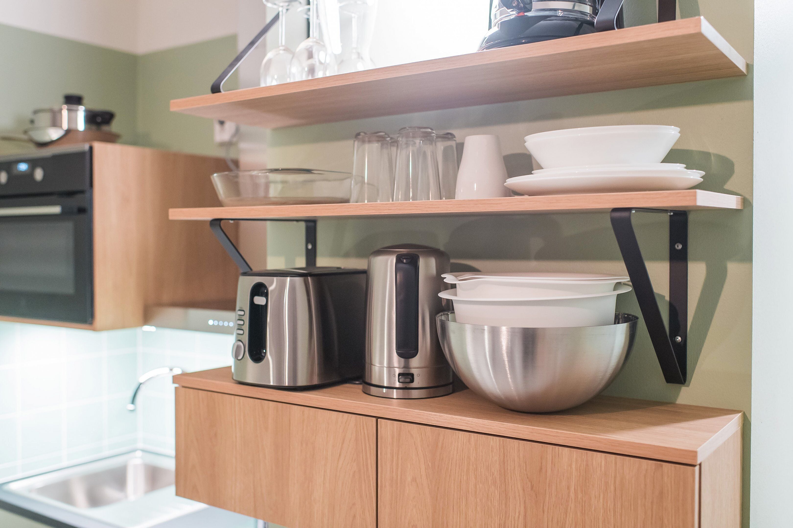 A kitchen with wooden cabinets, stainless steel appliances, and glassware on shelves.