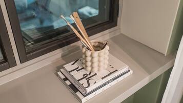Un rebord de fenêtre orné d’un récipient en céramique décoratif contenant des pinceaux et des crayons, ainsi qu’une pile de magazines ou de livres.