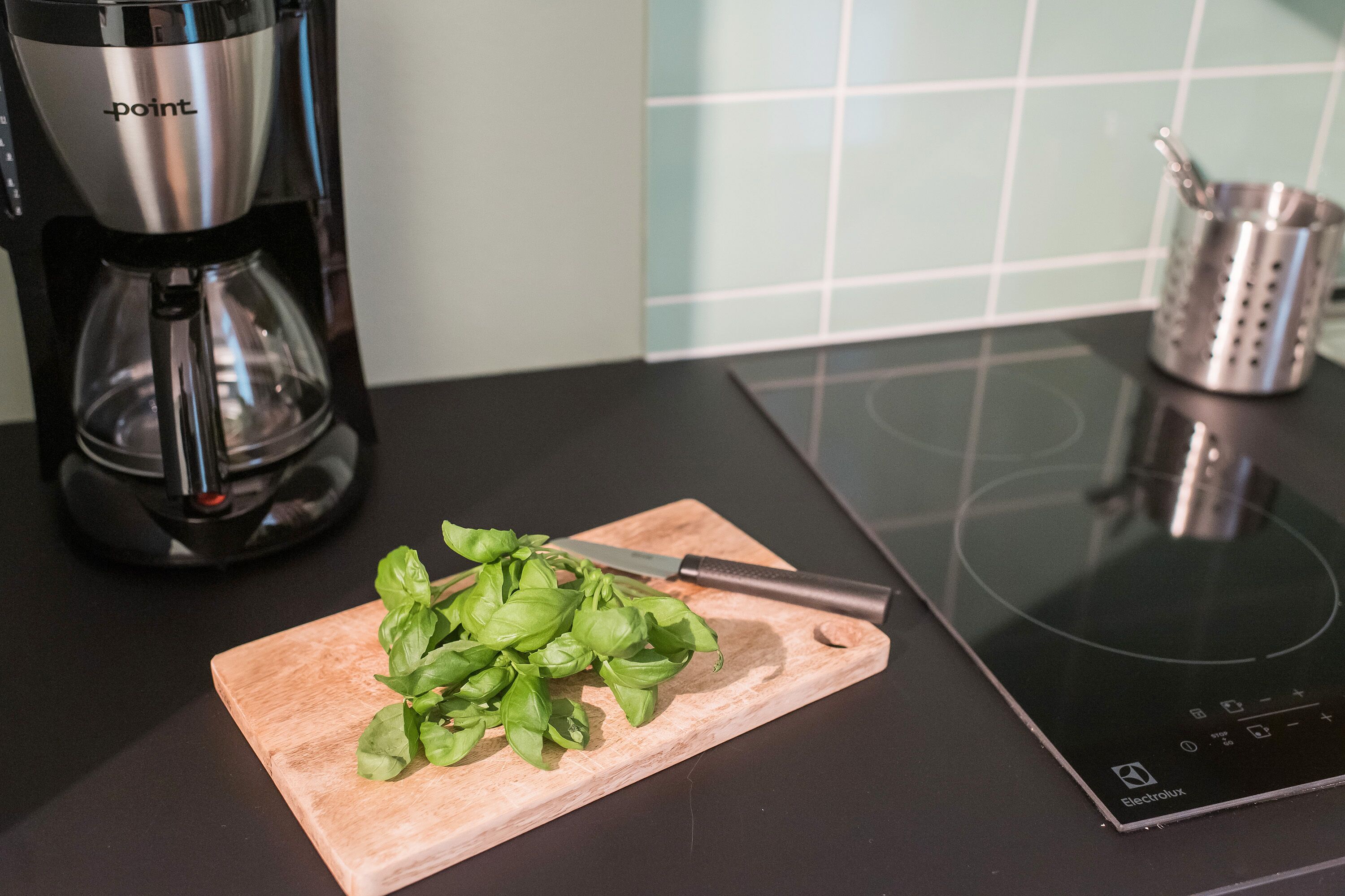 A kitchen with a coffee maker, a cutting board with basil, and a knife.